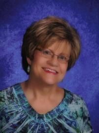 Smiling woman with glasses in blue patterned top against a purple background