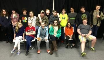 Youth group posing indoors in two rows on a stage, with some seated and some standing.