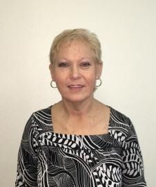Woman in a black-and-white patterned top, smiling against a plain light background.