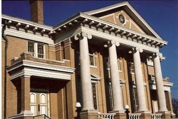 Brick building with tall white columns and a triangular pediment against a blue sky