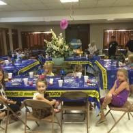 Children seated at a decorated banquet table in a hall with blue and yellow table settings