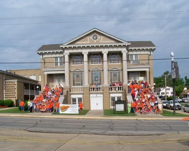 Historic building with columns and groups of people with orange shirts on both sides of the entrance.