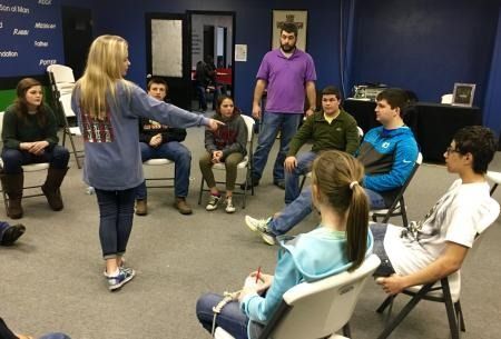 Group meeting in a classroom, with one person leading an activity as others sit in a circle.