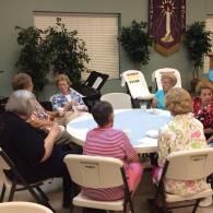 People seated around a round table in a community room, listening and talking during a meeting.