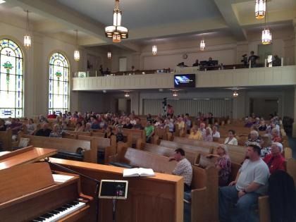 Church sanctuary with congregation seated in pews, viewed from the front near an organ and pulpit