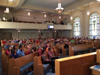 Congregation seated in a church sanctuary with stained-glass windows and a balcony during a service