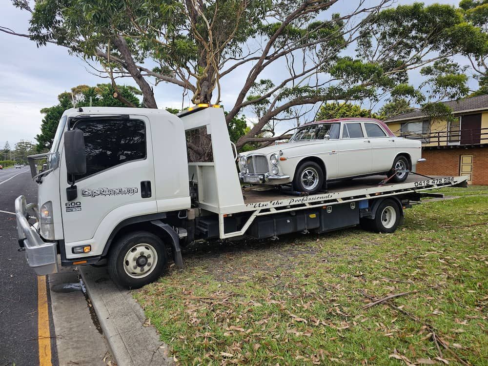 A White Tow Truck is Carrying a White Car on the Back of It — Optimum Towing in Culburra Beach, NSW