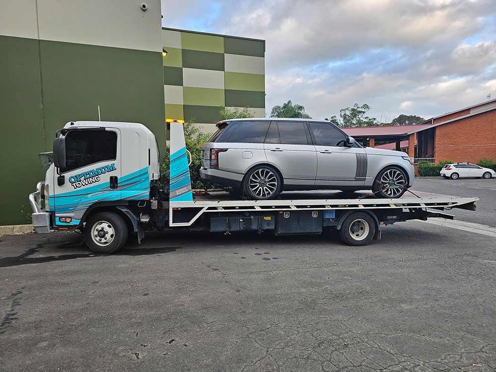 A Silver Range Rover Is Being Towed By A Tow Truck — Optimum Towing in Bomaderry, NSW