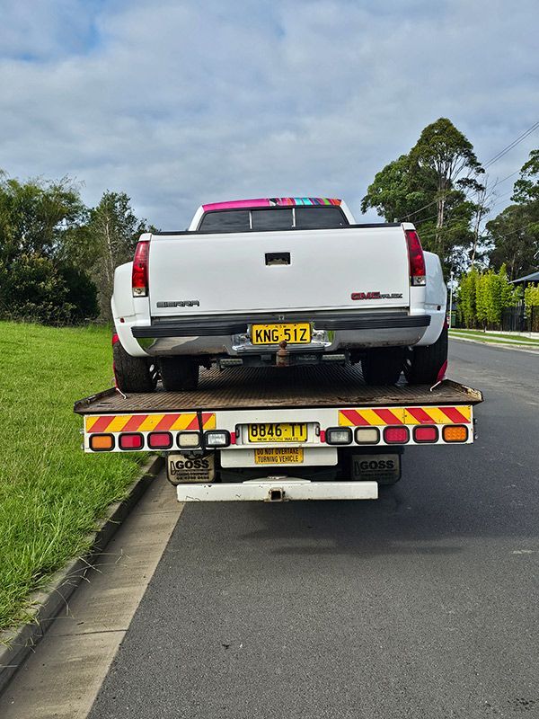 A Tow Truck Is Towing A White Pickup Truck Down The Road — Optimum Towing in Nowra, NSW
