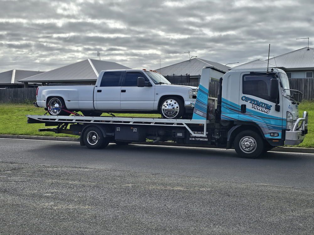 A White Pickup Truck Being Towed by a Tow Truck on a Residential Street — Optimum Towing in Bomaderry, NSW