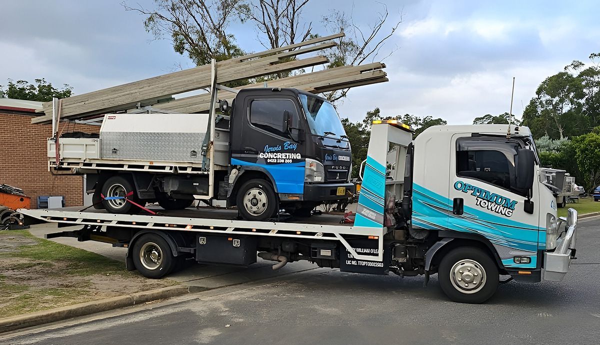 A White Tow Truck Is Carrying A Smaller Blue And Black Service Truck