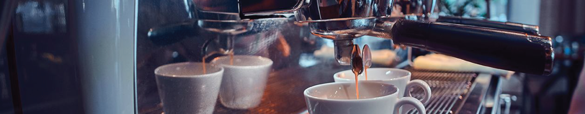 Espresso machine pouring coffee into cups on a café counter, with steam and warm lights