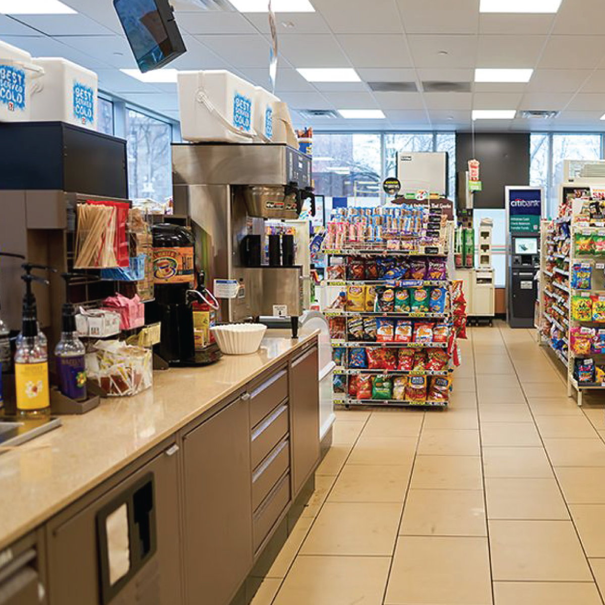 Convenience store interior with snack racks, coffee station, and tiled aisles under bright ceiling lights
