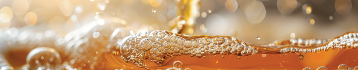 Close-up of sparkling amber liquid with bubbles and foam splashing across the surface