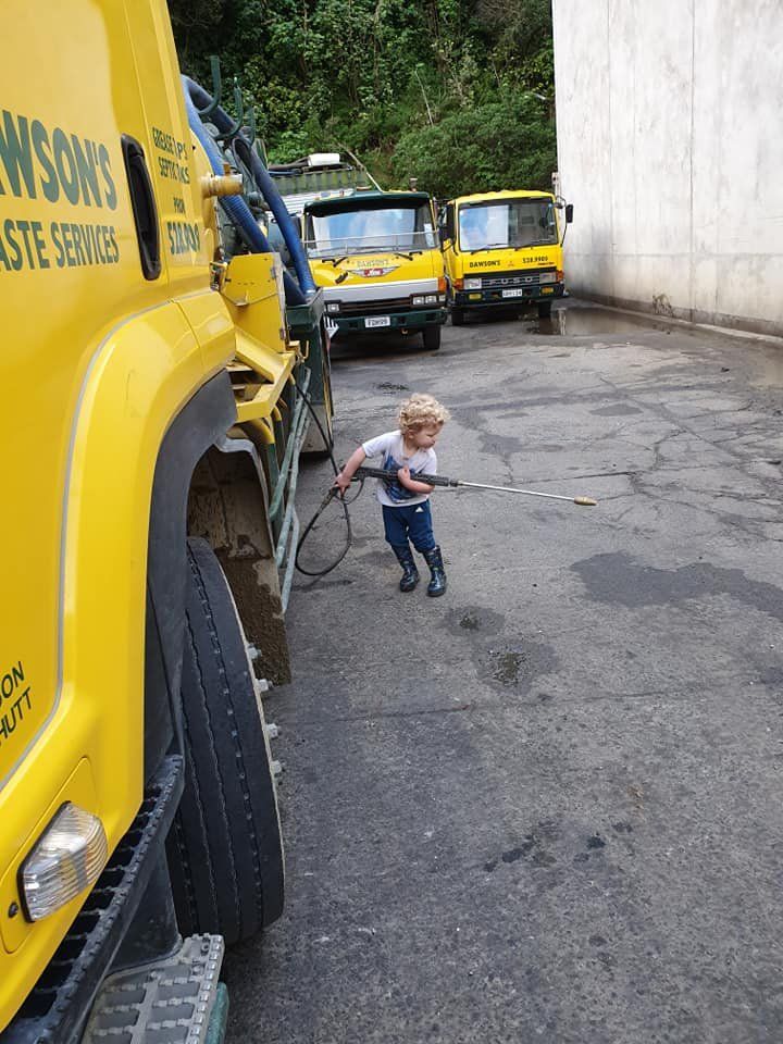 A little boy is standing in front of a yellow truck.