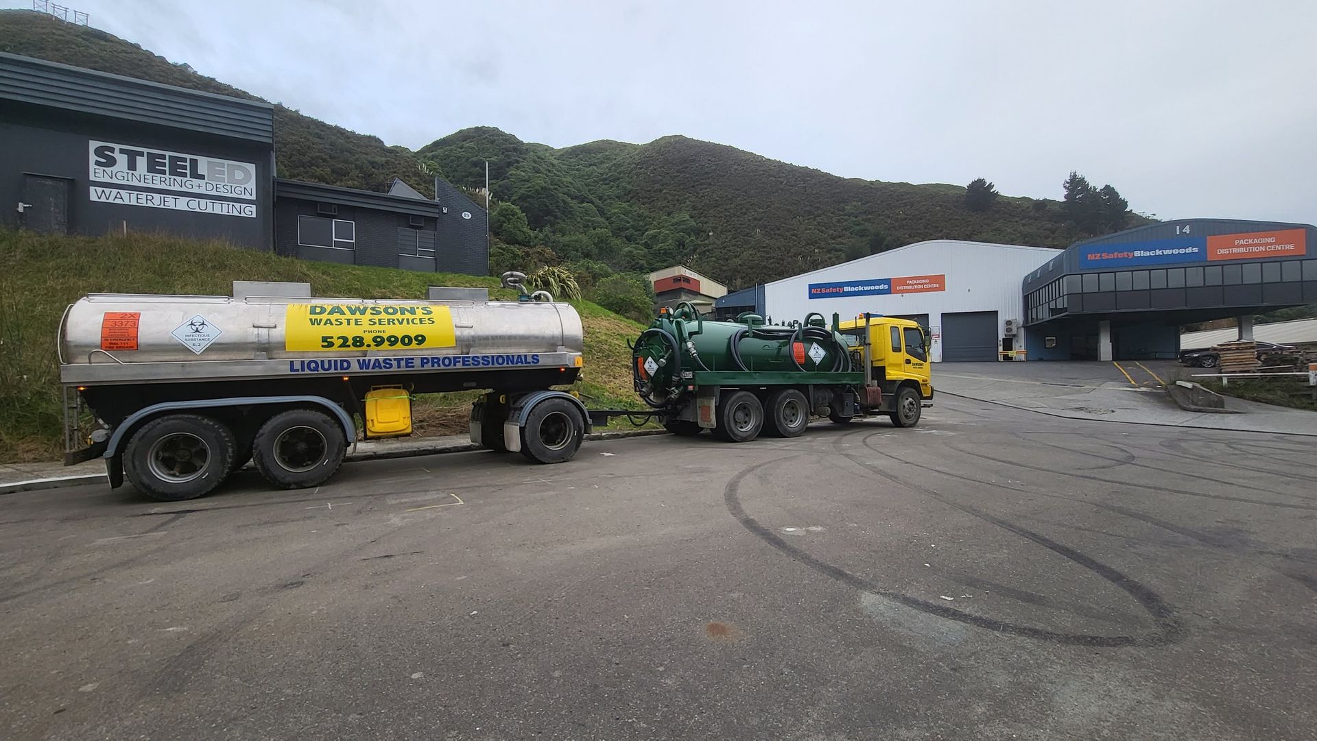A tanker truck and a vacuum truck are parked in front of a building.