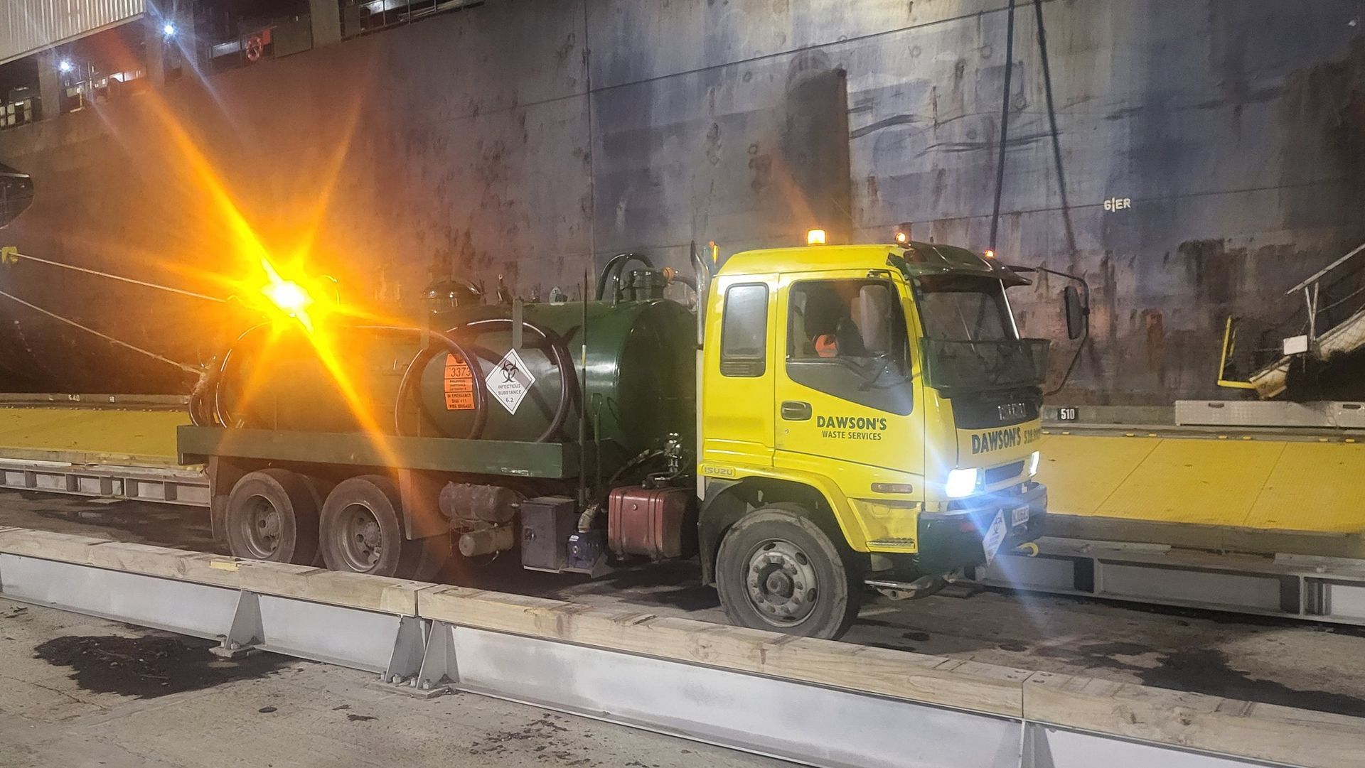 A yellow truck is parked on the side of the road at night.