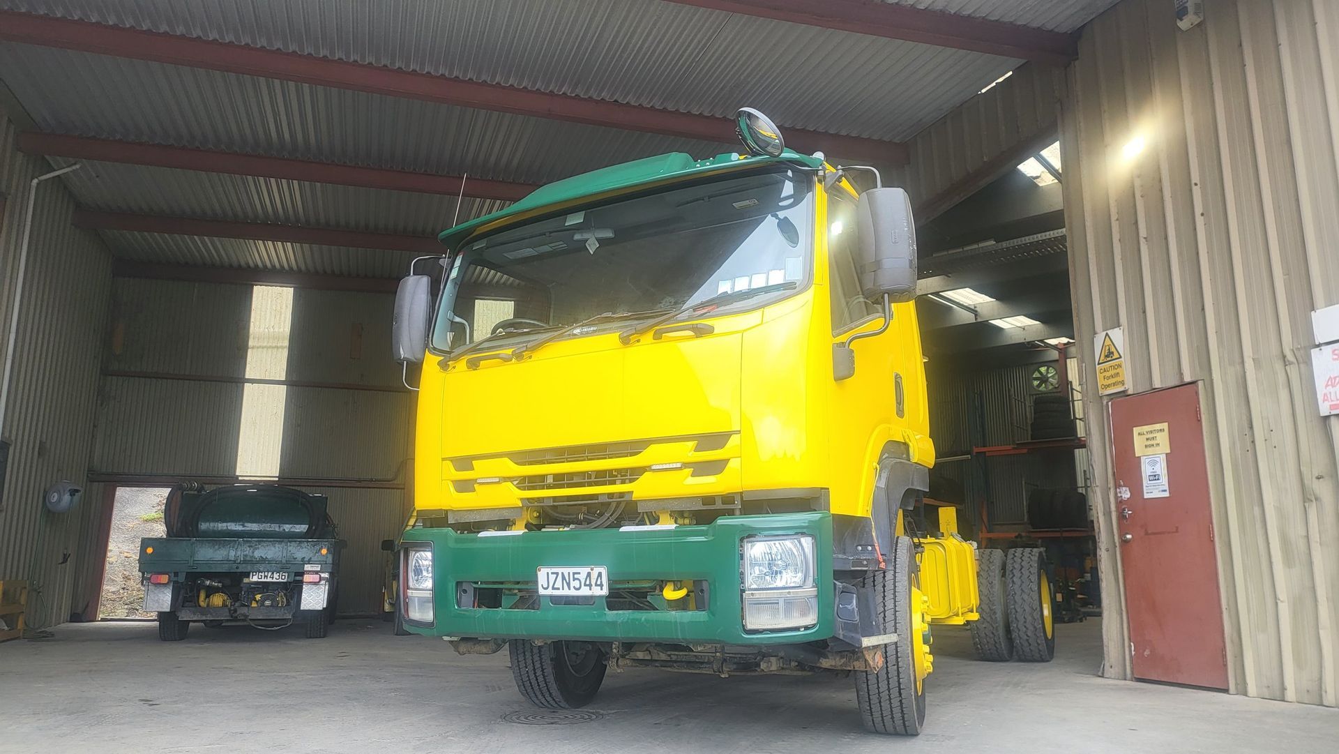 A yellow truck is parked in a garage next to a green truck.