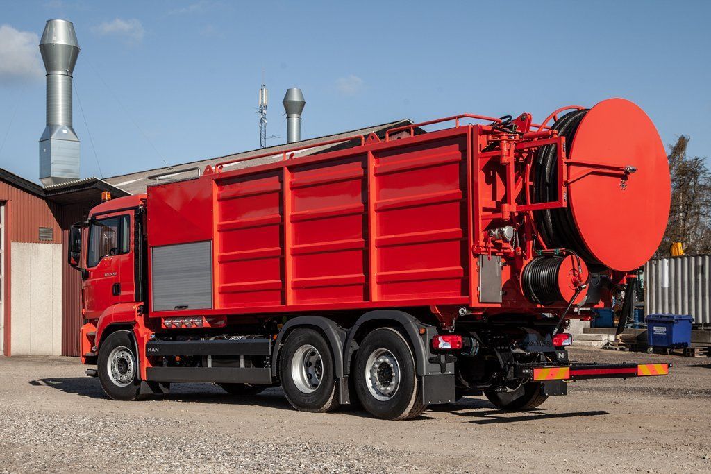 A red truck is parked in a gravel lot in front of a building.