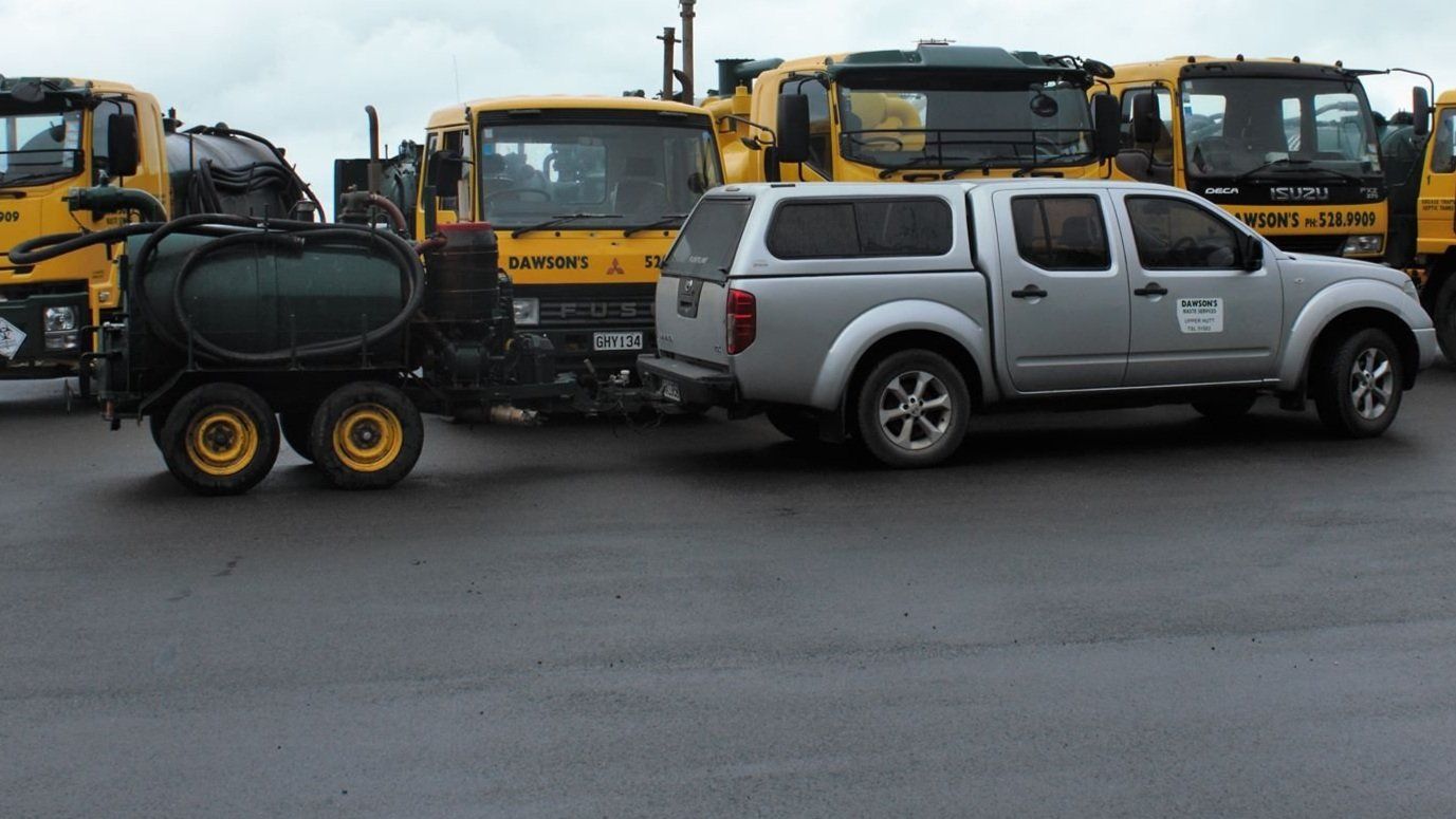 A truck with a trailer attached to it is parked next to a row of yellow trucks.