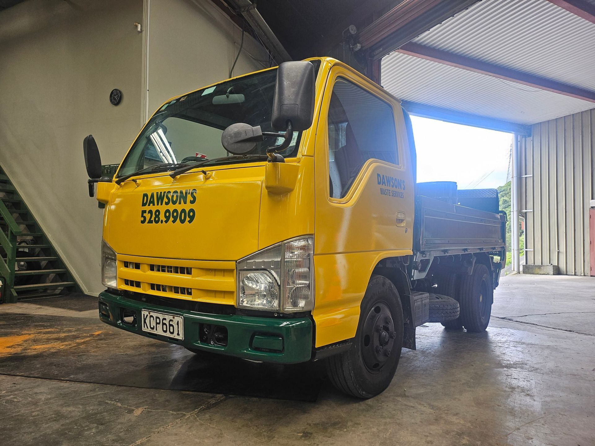 A yellow truck is parked in a garage with stairs in the background.