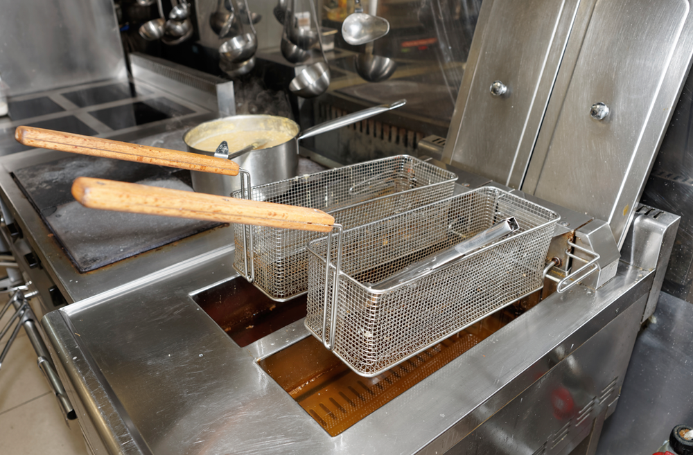 A stainless steel fryer with two baskets filled with oil.