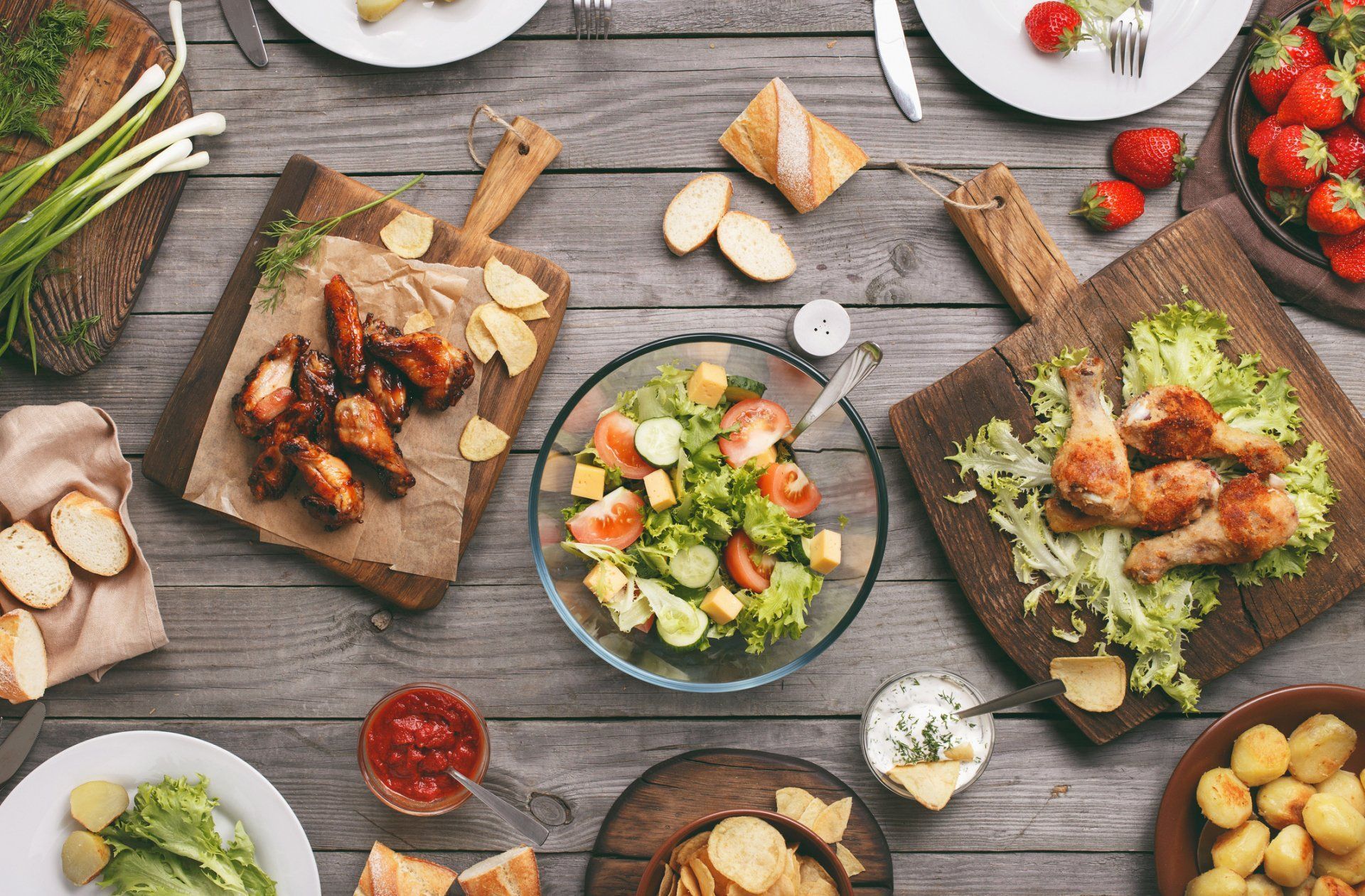 Overhead view of a rustic table with assorted dishes, salads, bread, and grilled meat on wooden boards