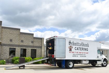 White catering truck parked at a stone building with a ramp, under a cloudy sky