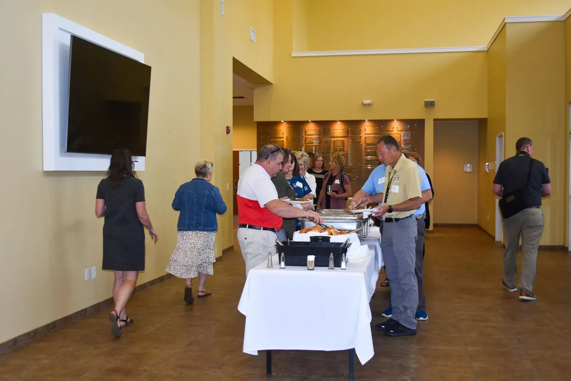 People gathered at a buffet table in a yellow indoor lobby or conference hall.