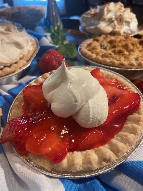 Strawberry tart with whipped cream topping on a tray, with other desserts blurred in the background.