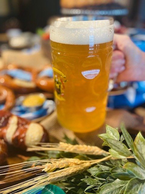 Tall beer glass with foam on a table, surrounded by bread, olives, and greenery