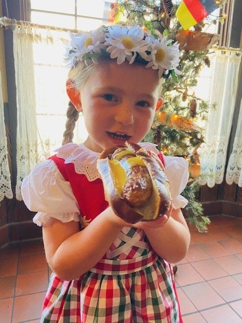 Child in a flower crown holding a pastry indoors near a decorated window.
