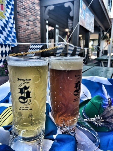 Two cocktails on a table outdoors, one pale yellow and one pink, with a city street background