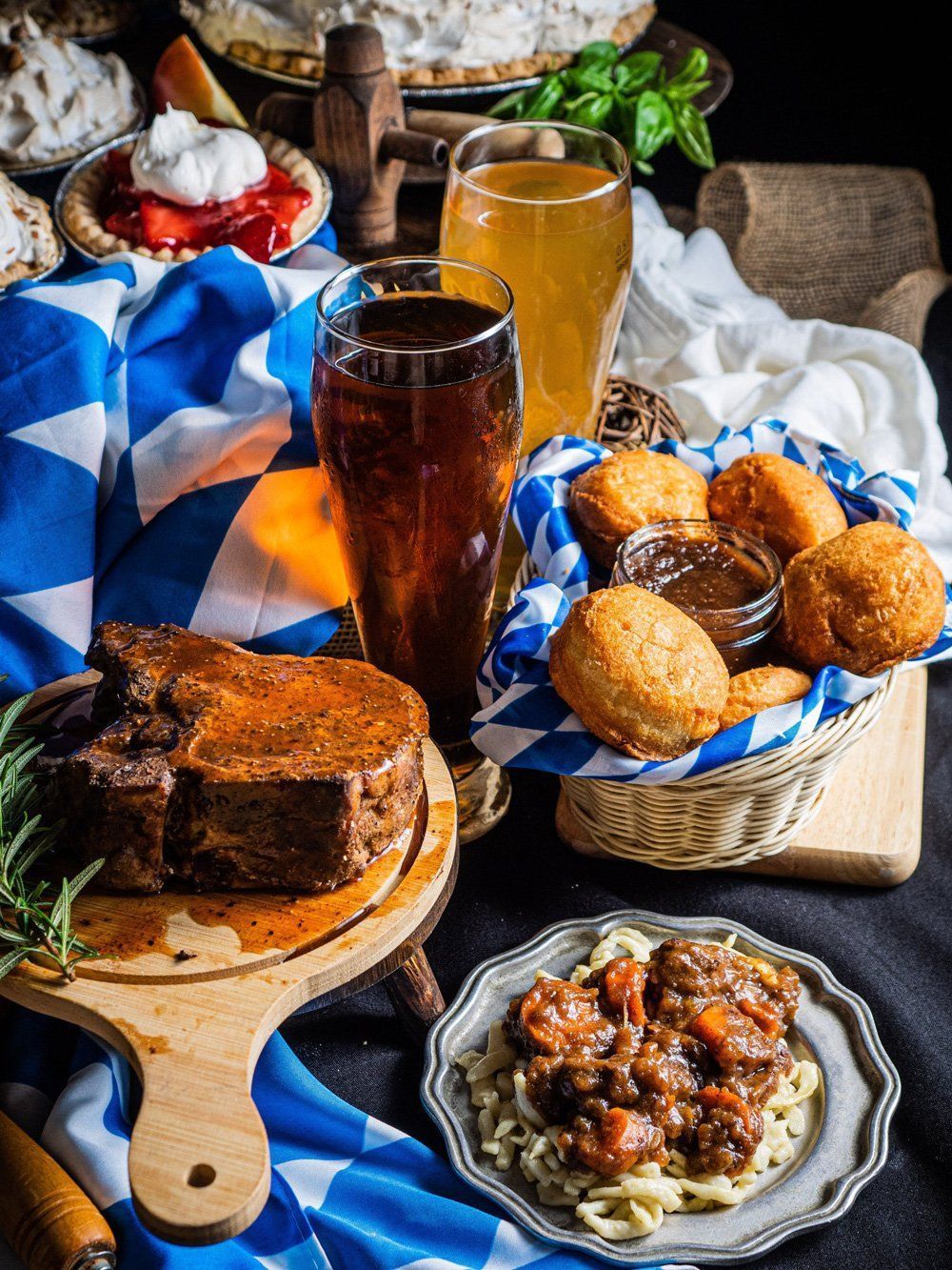Rustic breakfast spread with pastries, fried dough, jam, bread, and drinks on a blue-and-white cloth