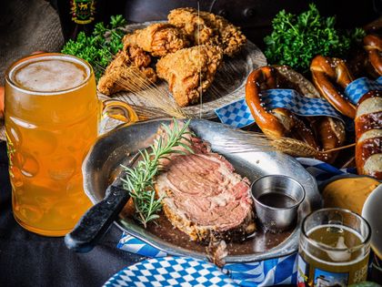 Beer and fried foods on a rustic table, with steak, pretzels, and a glass mug of beer