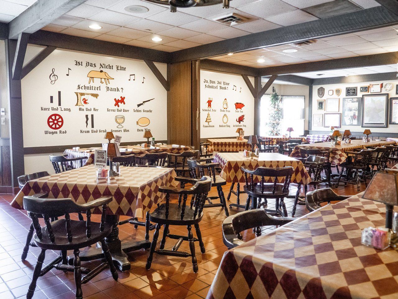 Rustic restaurant dining room with checkered tablecloths, wooden chairs, and wall decor on white walls.