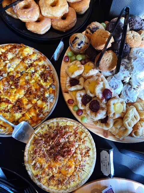 Assorted pizzas, bagels, and pastries on trays at a buffet table