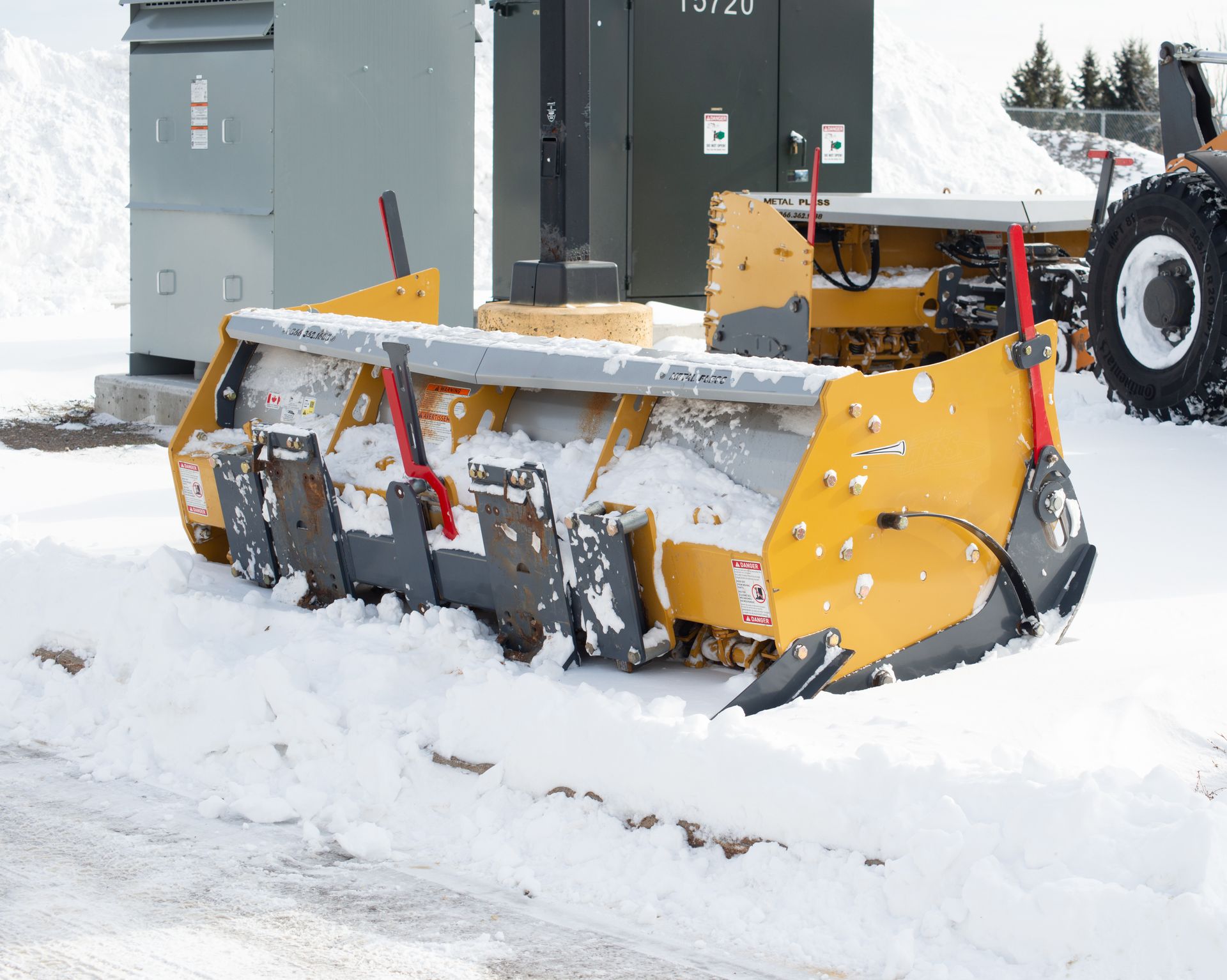 Yellow snowplow clearing snow beside a utility building on a snowy street