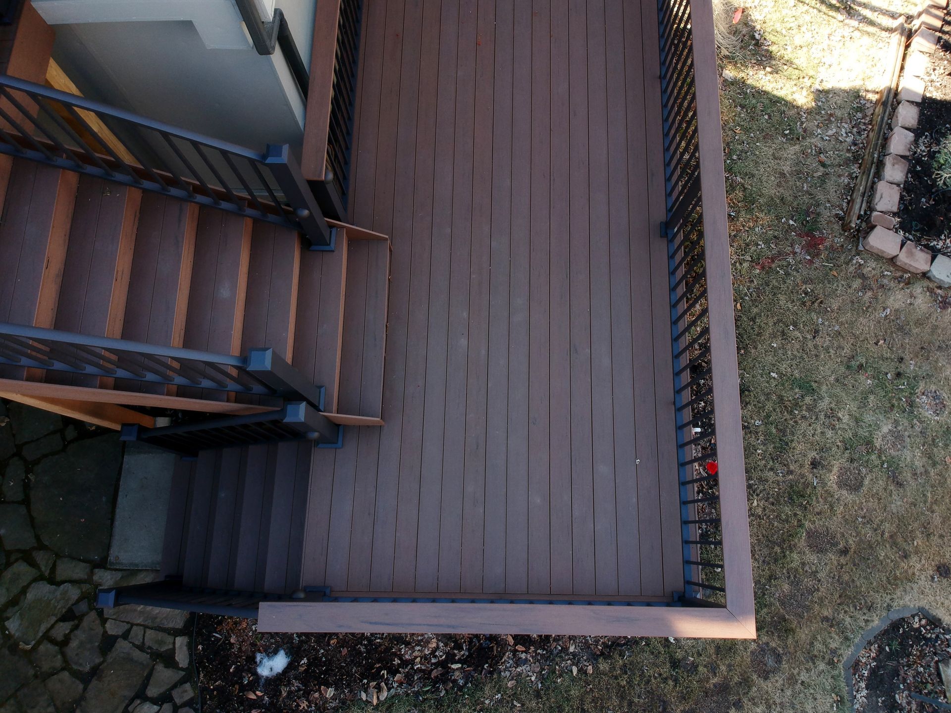 Top-down view of an outdoor wooden deck with stairs, railing, and adjacent grass.
