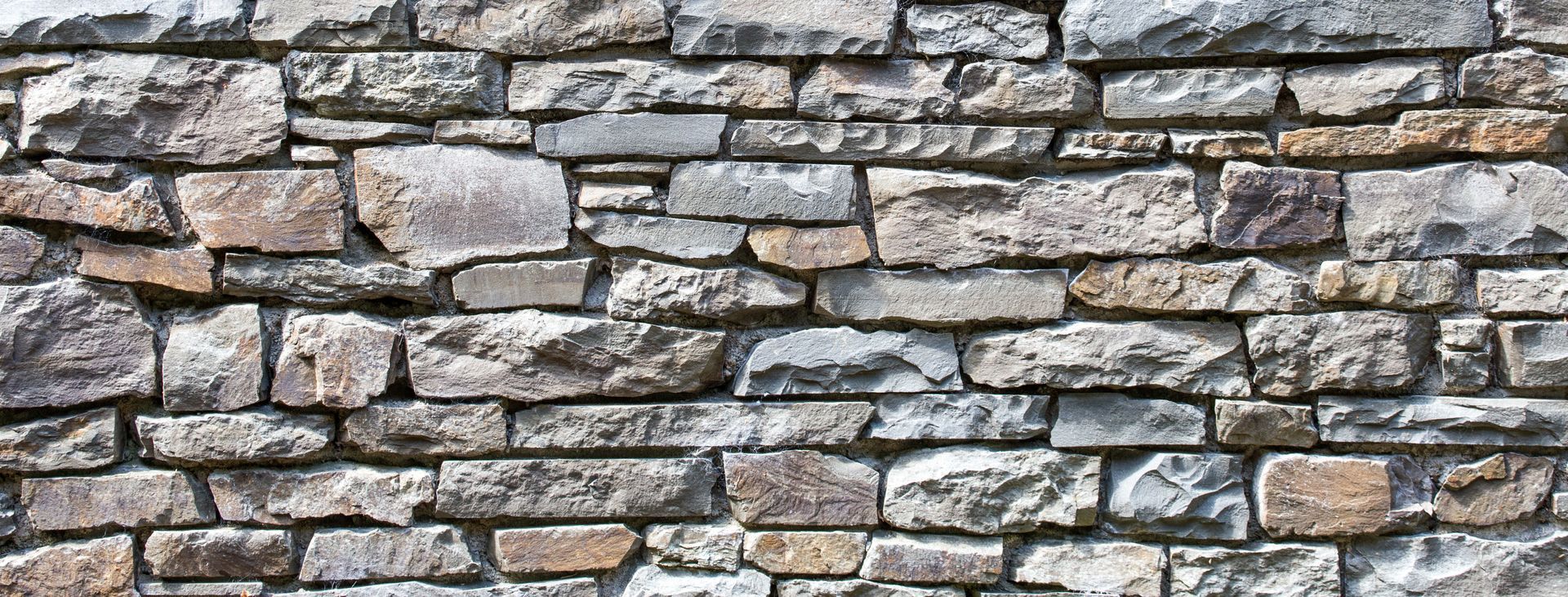 Gray stacked stone wall with irregular rectangular blocks and mortar joints