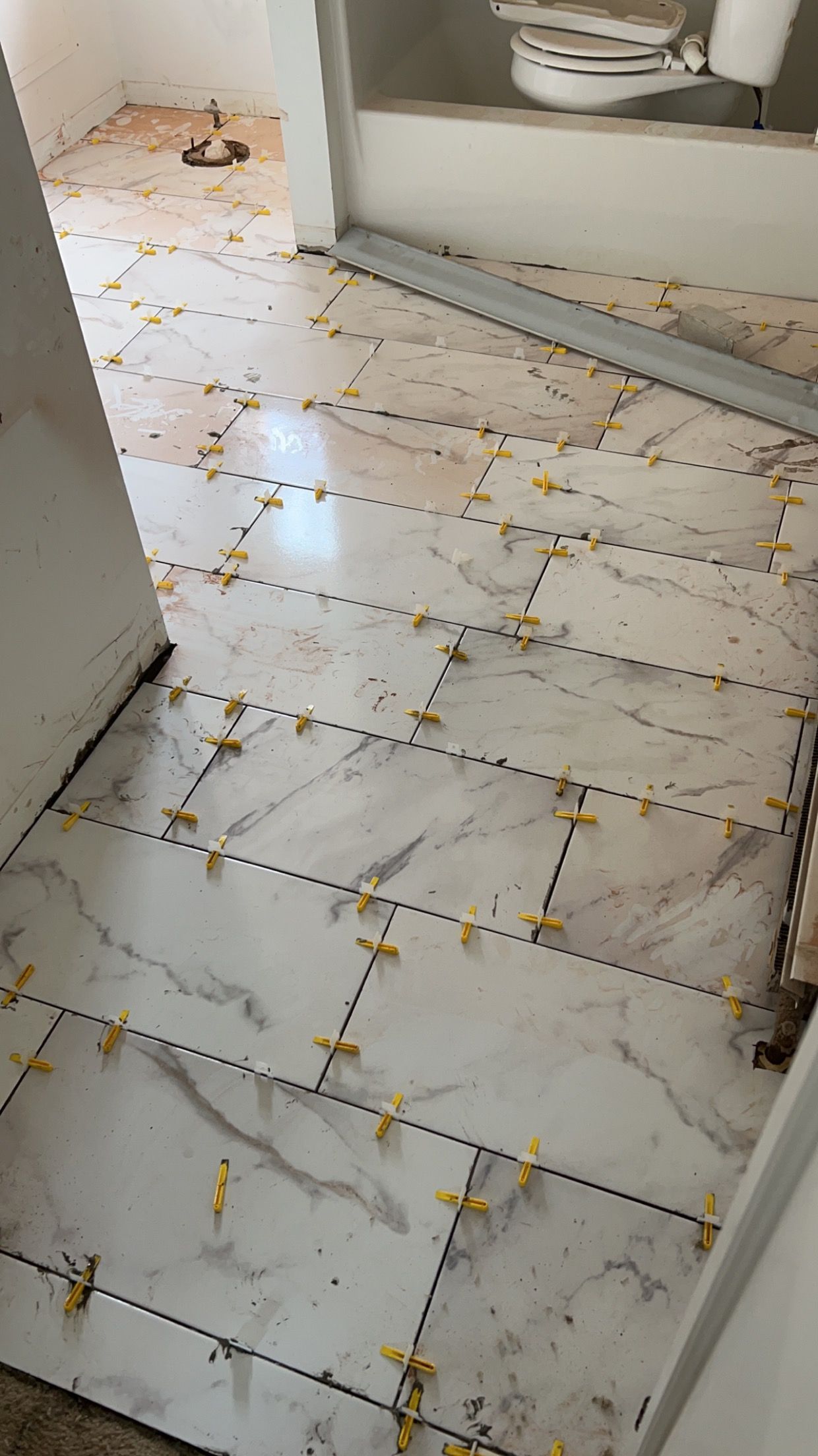 White tiled floor and wall with scattered yellow crumbs near a doorway or bathroom sink area