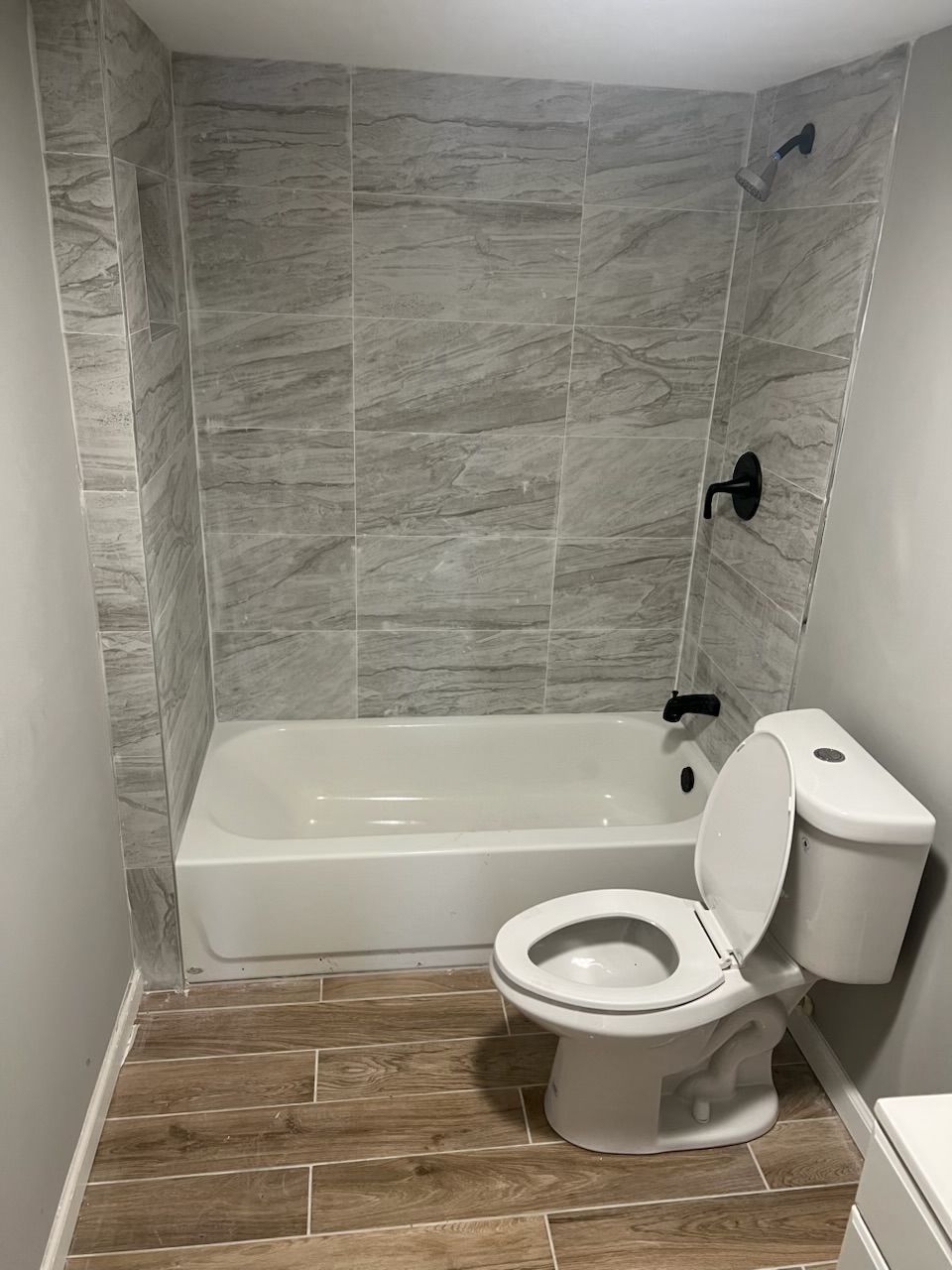 Small bathroom with a white toilet, bathtub, and gray tiled shower walls.