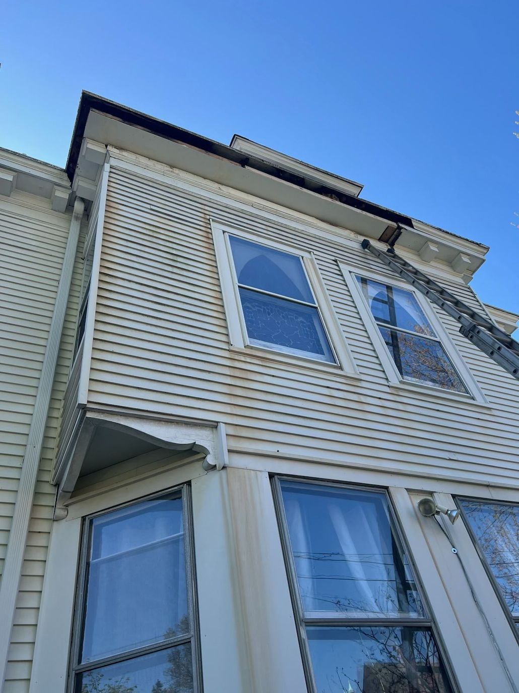 Upward view of a white house exterior with blue-tinted windows under a clear blue sky