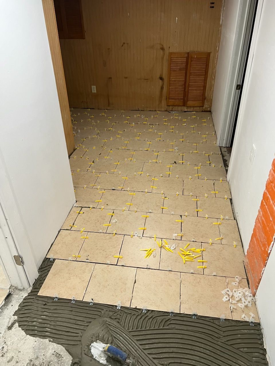 Partially tiled hallway floor with scattered yellow debris and unfinished wall trim