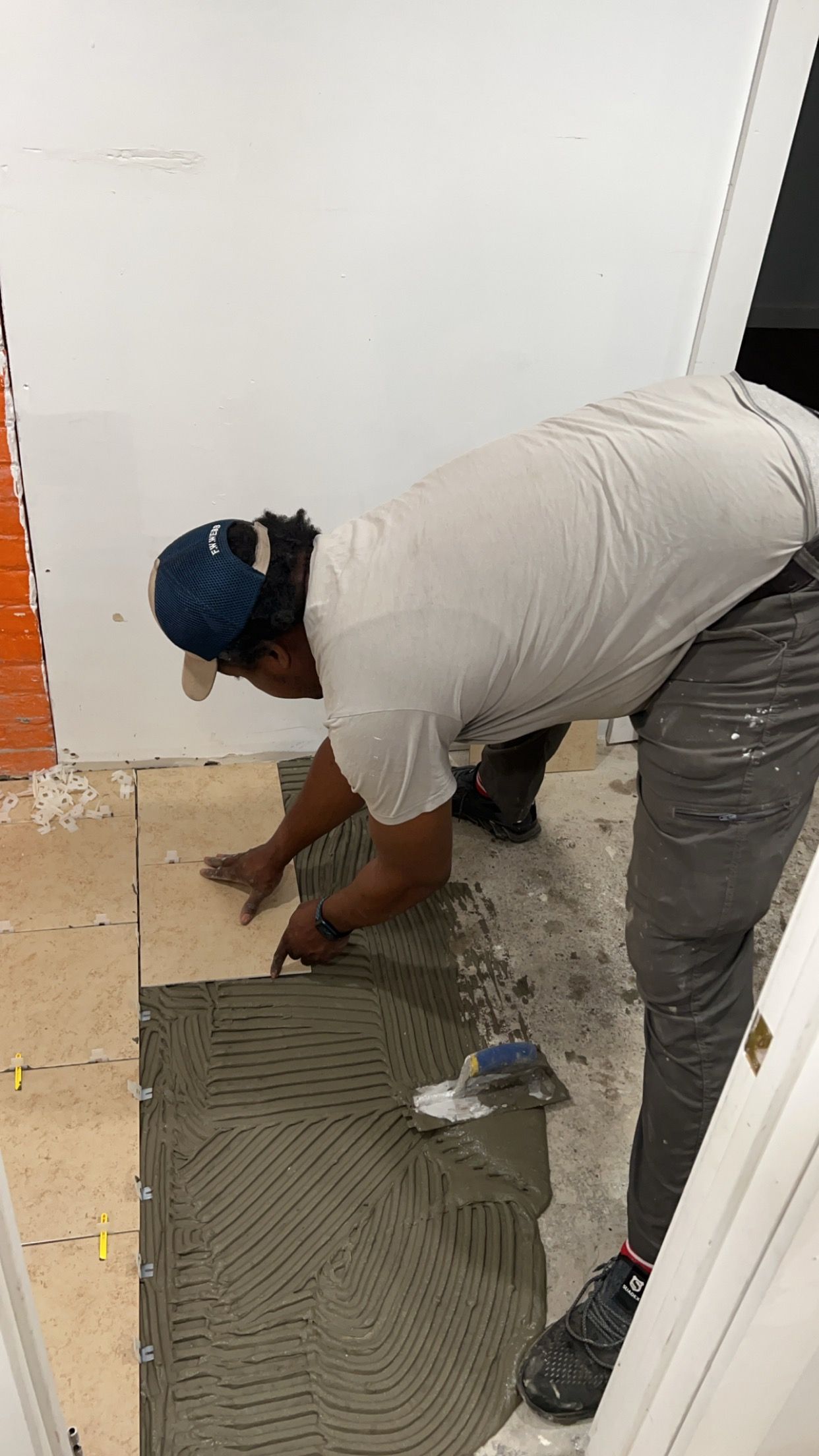 Worker kneeling on a floor, smoothing adhesive with a trowel during tile installation.