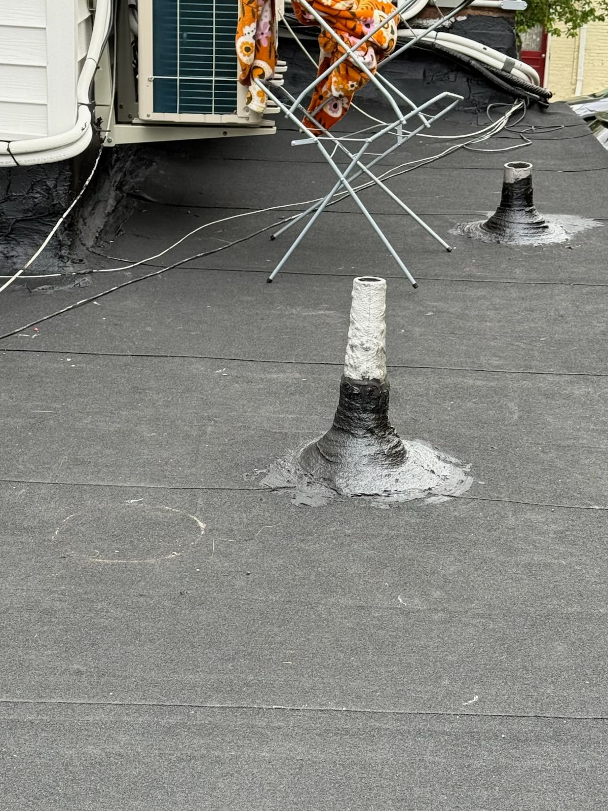 Rooftop with two vent pipes, coiled barbed wire, and a wall-mounted air conditioner unit