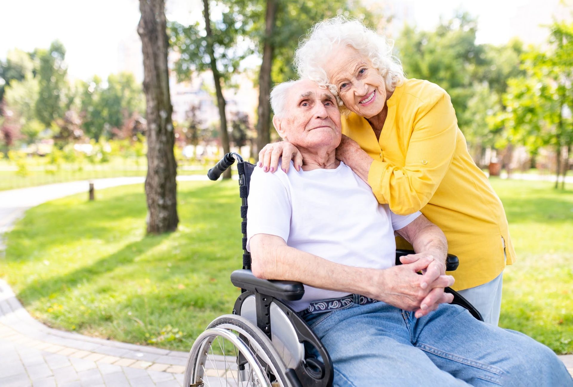 Older woman in a wheelchair with a smiling companion in a yellow sweater in a sunny park