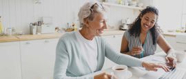 Two women smiling and talking over coffee at a bright kitchen table