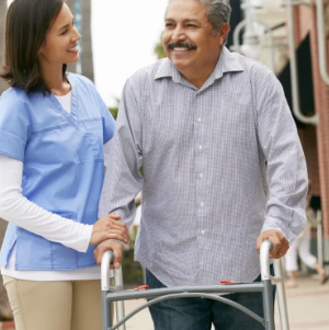 Nurse helping a smiling man with a walker on a sidewalk outside a building