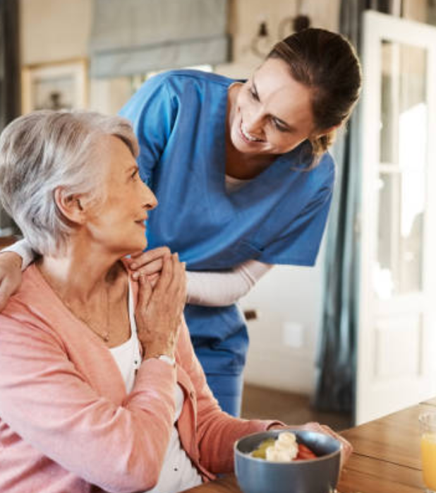 Caregiver helping an elderly woman drink water in a bright home setting